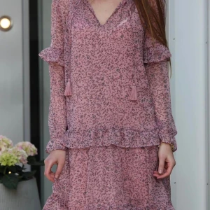 Rosa blommig klänning med volanger - Neo Noir klänning med blommigt mönster och volangdetaljer. Den har långa ärmar och en v-ringad hals med knytband. 