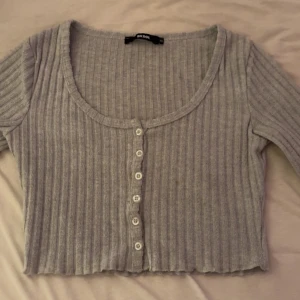 Grå ribbad topp från Bik Bok - Säljer en super gullig grå ribbad topp i storlek XS från Bik Bok. Den är croppad med knappar framtill och har långa ärmar. Frakt ingår i priset 