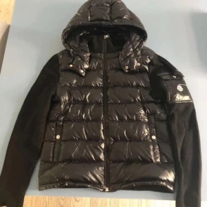 Svart moncler cardigan (gammal modell) - Snygg svart cardigan från Moncler med stickade ärmar och en luva man kan knäppa av. Perfekt för kyliga dagar!