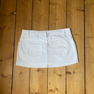 Mini jeanskjol  - Snygg vit kortkjol med praktiska fickor både fram och bak. Kjolen har en klassisk design med knapp och dragkedja framtill. Perfekt för en stilren look. Kort i modellen, low waist! 