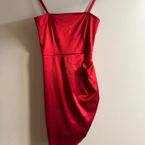 Röd kort klänning - Snygg röd klänning med smala axelband och en figurnära passform. Klänningen har en draperad detalj på sidan som ger en elegant touch. Perfekt för en kväll ute eller en speciell tillställning.