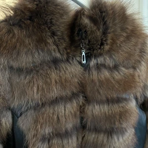 Brun pälsjacka med skinn - Snygg brun pälsjacka med skinninslag och dragkedja framtill. Jackan har en lyxig look med fluffig päls och quiltade detaljer i skinn. Perfekt för att hålla sig varm och stilren under kyliga dagar. Funkar som en S/M, utan märke, äkta päls och läder. 