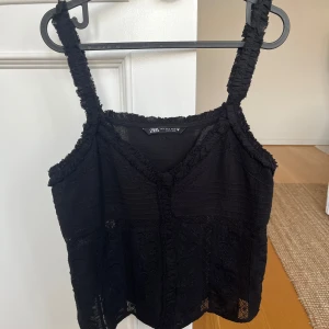 Svart topp från Zara - Snygg svart topp från Zara med breda axelband och v-ringning. Toppen har fina spetsdetaljer och broderade mönster. Använd fåtal gånger och i mycket gott skick🖤