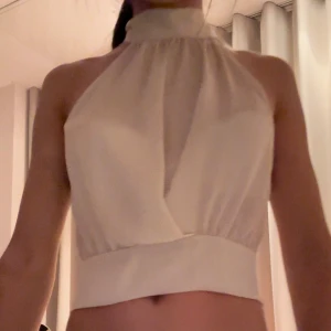 Vit halterneck topp - Snygg vit halterneck topp med knytning i nacken. Toppen är ärmlös och har en croppad passform, perfekt för sommarens varma dagar eller för att få en stilren outfit💕