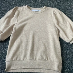 Beige tröja med puffärmar - Säljer en stilren beige tröja med puffärmar. Tröjan har en rund halsringning och är tillverkad i ett mjukt material. Perfekt för en avslappnad look.