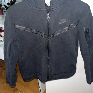 Svart nike tech  - Snygg svart Nike tech  med dragkedja och huva. Storlek M i barnstorlek. Inköpt för 1000kr. Priset är öppet för diskution