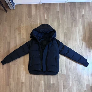 Canada goose jacka macmillan - Snygg svart pufferjacka med huva och dragkedja. Svart canada goose loga,  Perfekt för kalla dagar med sin quiltade design från canada goose. Jackan har en stilren look och är idealisk för vinter och höst.