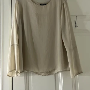 Beige blus från Gina Tricot - Säljer en  beige blus från Gina Tricot. Blusen har långa ärmar och en rund halsringning, perfekt för en elegant look. Materialet är mjukt och bekvämt, vilket gör den idealisk för både vardag och speciella tillfällen.