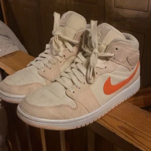 Nike Air Jordans med orange Swoosh - Snygga Nike Air Jordans i beige med en iögonfallande orange Swoosh. Skorna har snörning och är tillverkade i ett texturerat material som ger en unik look.