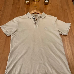 Burberry piké - Pikétröja från den fina märket burberry i en grå färg. Tröjan är i fint skick och har inga deffekter! Tröjan är i storlek L men passar M/L skulle jag säga. Tröjan är köpt för 2000 cirka ett år sedan. Vid fler frågor är det bara att kontakta mig!