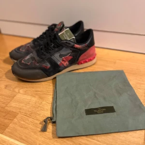 Valentino rockrunners - Snygga Valentino Garavani sneakers med kamouflagemönster i rött och svart. De är storlek 41 men passar 42. Skorna är självklart äkta och är köpta på northstarhorizon.store. Den är i dåligt skick (defekter kan ni se på bild 3,4 och 5). Vänstra skon har tidigare varit sönder där fram och har blivit fixad på sko makaren. Skorna kommer med en dustbag. Om ni har några frågor eller vill ha fler bilder är det bara att kontakta mig.👍