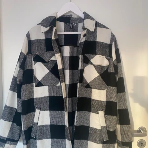 Svartvit rutig overshirt från H&M - Snygg och trendig svartvit rutig overshirt från H&M. Perfekt för lager-på-lager-stil med knappar framtill och två bröstfickor. Den har en klassisk krage och långa ärmar. Den är inte så varm så skulle rekommendera till vår/höst. Kontakta för mer bilder!