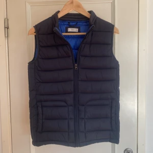 Mörkblå dunväst från MNG - Snygg mörkblå dunväst från MNG med dragkedja framtill. Västen har en quiltad design med en kontrast färg i. Strl XS. Skick 8/10. 
