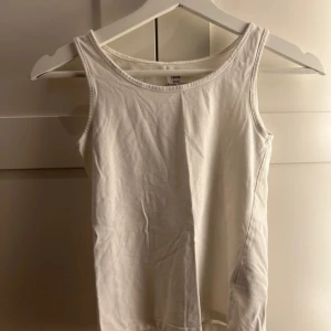 Vit linnetopp från H&M - Säljer en enkel och stilren vit linnetopp från H&M i ekologisk bomull. Perfekt för en avslappnad look. Toppen har en klassisk rund halsringning och är ärmlös.