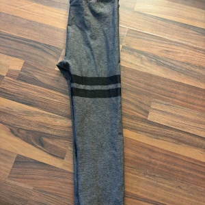 Grå leggings från Stronger - Snygga grå leggings från Stronger med svarta ränder runt benen. Perfekta för träning eller en avslappnad dag. De har en bekväm passform och är tillverkade i ett stretchigt material.