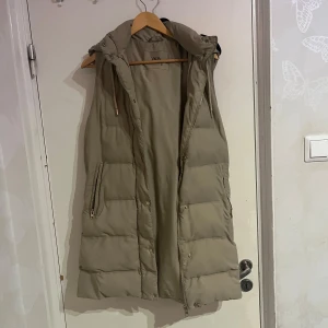 Beige dunväst från Zara - Säljer en snygg beige dunväst från Zara. Västen har en dragkedja framtill och praktiska fickor på sidorna. Perfekt för lager-på-lager under kyligare dagar.