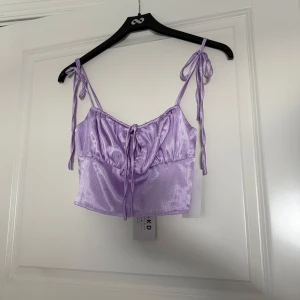 Lila satinlinne från NA-KD - Snygg lila satinlinne från NA-KD med knytband på axlarna och en liten rosett framtill.