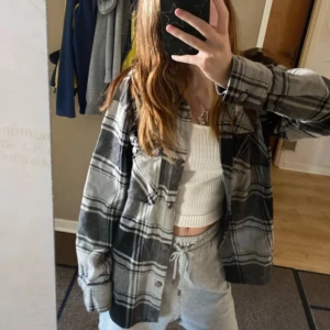 Grå och svart rutig overshirt - Snygg och bekväm grå och svart rutig overshirt med knappar. Perfekt för lager-på-lager stil. Passar bra till både avslappnade och mer uppklädda tillfällen. Aldrig använd!