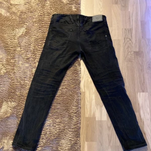 Svarta jeansbyxor från Replay - Snygga svarta jeansbyxor från Replay, modell Anbass. De har en klassisk femficksdesign och en knappgylf. Perfekta för en stilren look.