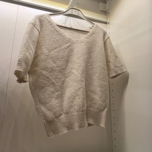 Beige stickad tröja med v-ringning - Mysig beige stickad tröja med v-ringning och korta ärmar. Perfekt för en avslappnad stil med ribbade kanter som ger en fin passform.