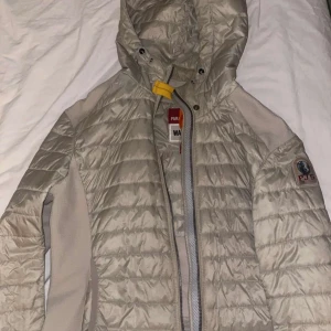 Beige jacka från Parajumpers - Säljer en snygg beige jacka från Parajumpers med huva och dragkedja. Jackan har quiltade detaljer och en logotyp på ärmen. Perfekt för kyligare dagar. Använts 2 gånger, skriv vilket pris ni hade kunnat buda