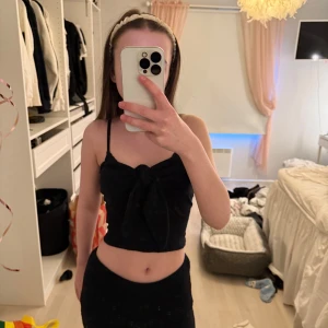 Svart croppad topp med knyt - Snygg svart croppad topp med knyt framtill. Den är ärmlös och perfekt för varma dagar eller en utekväll. Enkel och stilren design som passar till det mesta.