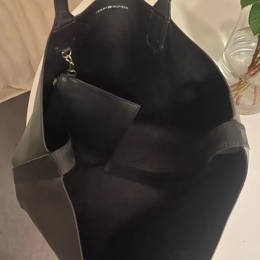 Snygg och rymlig svart shoppingväska från Tommy Hilfiger i skinn. Väskan har ett elegant guldemblem på framsidan och en praktisk innerficka med dragkedja. Perfekt för att bära med sig allt man behöver under dagen. Finns några rivmärken från kattis, men fungerar väl. Hör av dig om du vill ha tydligare bilder 🌸Nypris: 1695kr . Laukut & Käsilaukut.