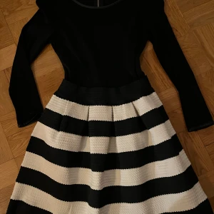Svart och vit randig klänning - Snygg klänning med svart överdel och randig kjol i svart och vitt. Klänningen har långa ärmar och en dragkedja i ryggen. Perfekt för en stilren look.