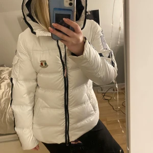 Vit dunjacka från Dolomite - Säljer en snygg vit dunjacka från Dolomite med svart dragkedja och logotyp på bröstet. Jackan har en hög krage och huva för extra värme. Perfekt för kyliga dagar! Tar även byten 