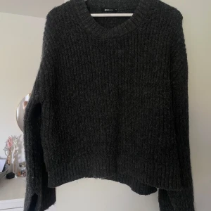 Stickad tröja från Gina Tricot - Mörkgrå stickad tröja från Gina Tricot i storlek M. Har slits vid ärmar och på sidorna  vid magen/midjan. Köpt förra hösten, använd ca 4-5 gånger.