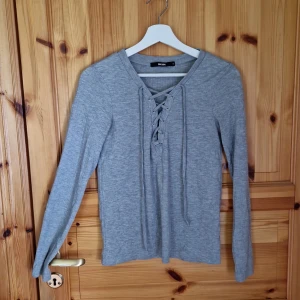 Grå tröja med snörning - Säljer en stilren grå tröja från BIKBOK. Den är långärmad och har en snygg snörning framtill som ger en extra detalj. Perfekt för både vardag och lite mer uppklädda tillfällen. Tröjan är i bra skick och superbekväm att ha på sig!