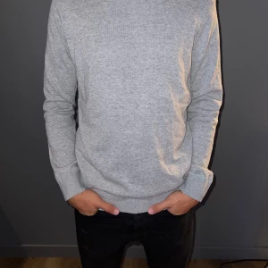 Stickad tröja (grå) - Tröjan är stickad och är i färgen grå. Det är en tunnare stickad tröja som används mycket lite. Storleken är L men passformen är lite mindre.
