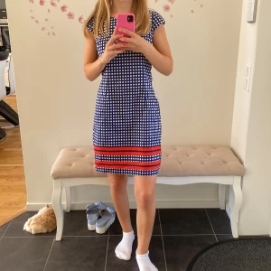 Blå och vit rutig klänning med röda detaljer - Säljer en superfin blå och vit rutig klänning med röda ränder längst ner. Den är kortärmad och har en tight passform som framhäver figuren. Perfekt för sommarens fester eller en dag på stan!