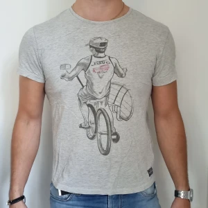 T-shirt med tryck  - Grå T-shirt med ett snyggt tryck av 100% bomull, från Jack & Jones. Något mindre än en traditionell stl. L. Fint skick och skönt material.  