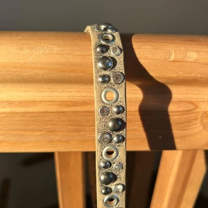 Beige bälte med nitar - Snyggt beige bälte dekorerat med glittriga nitar i olika storlekar. Perfekt för att ge en extra touch till din outfit. Bältet har ett klassiskt spänne i silverfärg✨🪩