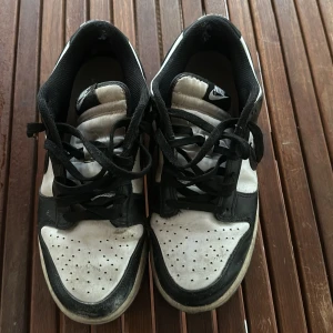 Svartvita Nike sneakers - Säljer ett par klassiska svartvita Nike sneakers med snörning. Skorna har en stilren design med svart Nike-logga på sidan och perforerade detaljer på tån. Perfekta för en avslappnad stil.