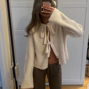 Stickad kofta med rosetter - Säljer en mysig beige stickad kofta med knytband framtill. Koftan har långa ärmar, endast använd 1 gång💞.