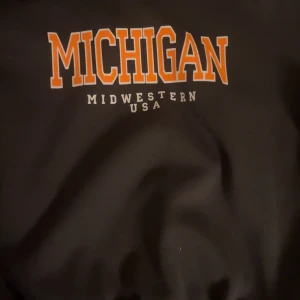 Svart tröja med motiv - Säljer en svart tröja från Shein med trycket 'Michigan Midwestern USA' i orange och vitt. Perfekt för en avslappnad stil. Tröjan har en klassisk passform och är tillverkad i ett mjukt material.