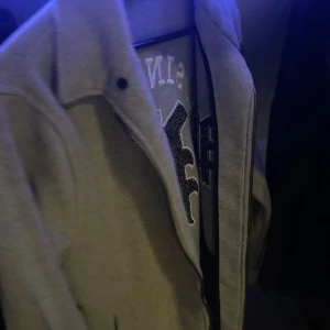 Grå collegejacka - Snygg beige jacka med tryck 'EST. SINCE 1992' och en stor bokstav på ryggen. Jackan har en klassisk krage och verkar vara i ett stilrent utförande. Perfekt för en avslappnad look.