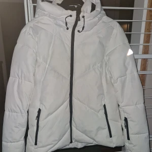 Vit dunjacka från McKinley - Säljer en snygg vit dunjacka från McKinley med huva. Jackan har praktiska fickor med dragkedjor för bland annat liftkort.