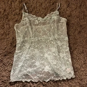 Ljusblått spetslinne - Säljer ett ljusblått spetslinne med tunna axelband. Linnet har ett blommigt mönster. Passar för att ha under en annan tröja då den är väldigt genomskinlig 