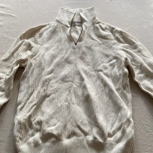 Beige stickad tröja från Zara - Säljer en stilren beige stickad tröja från Zara med dragkedja vid halsen. Perfekt för kyligare dagar med sin ribbade struktur och långa ärmar. En klassisk och mångsidig tröja för garderoben.