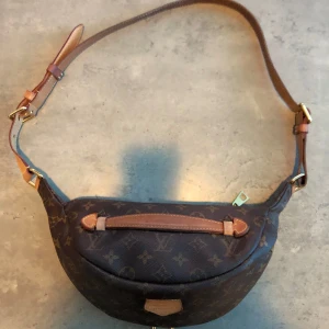  Louis Vuitton BumBag - En LV BumBag som är inköpt från Vinted för ca 2 månader sen. Väskan har tyvärr inte kommit så mycket till användning som jag ville. Väskan är i ett bra skick men kom en repa när jag beställde den (se bild) det är inget man ser eller nåt som stör väskans funktion. Fick inte med något kvitto men resterade grejer(låda, tygkasse mm medföljer. Fler bilder skickas privat då Max är 5 bilder här