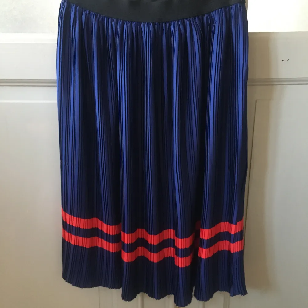 Snygg blå plisserad kjol från Saint Tropez med röda ränder längst ner. Perfekt för en stilren look. Resår i midjan för bekväm passform.. Hameet.