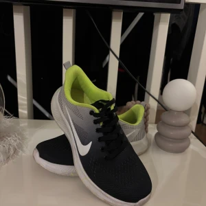 Nike sneakers med neongröna detaljer - Snygga Nike sneakers i svart och grått med neongröna detaljer. Skorna har en vit sula och klassisk snörning. Perfekta för en sportig look. Pris kan diskuteras