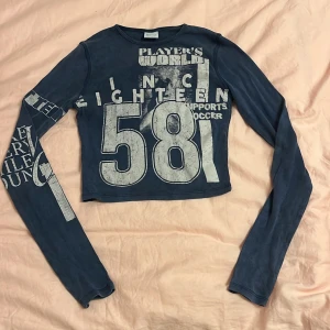 Blå croppad tröja från Bershka - Säljer en blå croppad tröja från Bershka med tryck i vitt. Tröjan har långa ärmar och en cool vintage-look med texten 'Player's World' och siffran '58' på framsidan. Perfekt för en avslappnad stil.