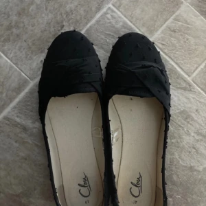 Svarta ballerinaskor med rosett - Eleganta svarta ballerinaskor med en dekorativ rosett på ovansidan. Skorna har en diskret prickig textur som ger en unik touch. Perfekta för en stilren look.