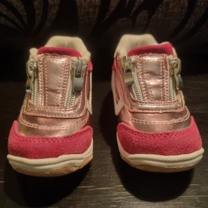 Nya Barnsneakers från Lejon i rosa och rosasilver med dragkedjor - Nya Snygga barnsneakers från Lejon i en kombination av rosa mocka och rosasilverfärgad syntet. Skorna har dragkedjor framtill för enkel på- och avtagning. Perfekta för små fötter som vill ha stil och komfort. Storlek 21