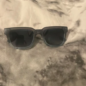 Svarta/gråa solglasögon från Komono - Snygga svarta solglasögon från Komono med en rektangulär form. De har en stilren design med mörka linser och en solid ram. Perfekta för att ge en cool touch till din stil.