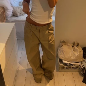 Beige kostymbyxor - Säljer ett par beige kostymbyxor med loose fit och låg midja. Byxorna har flera fickor och en avslappnad stil, perfekt för en trendig look.